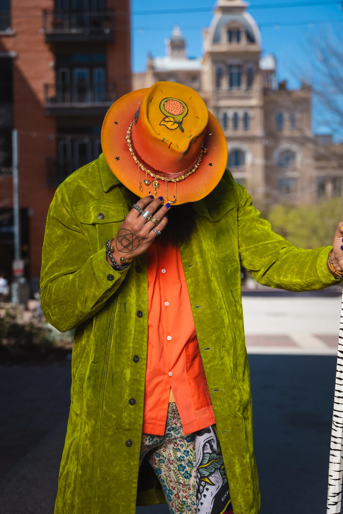 La Sombra in an orange custom hat and vivid green coat